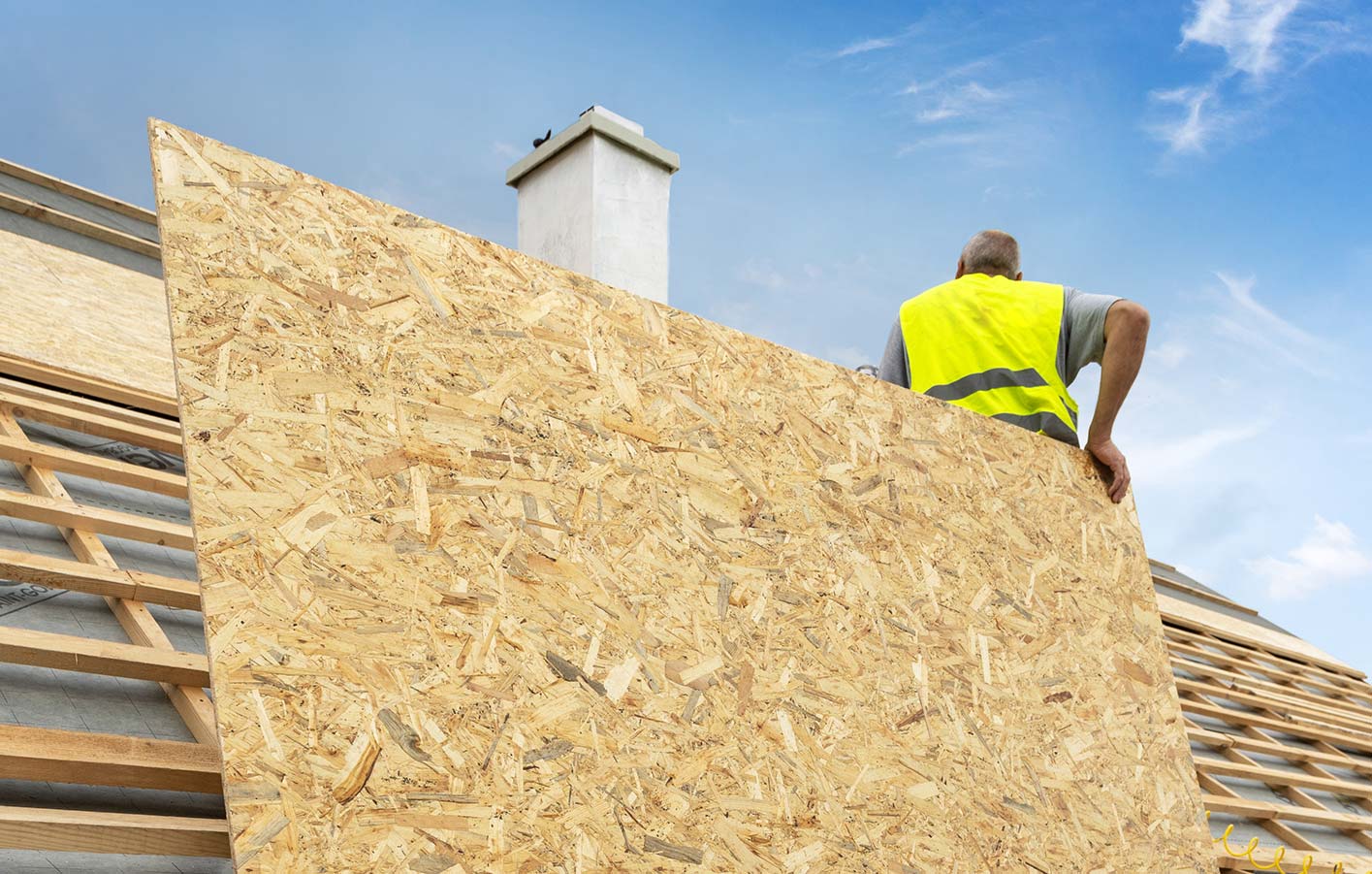 OSB-Platten statt Spanplatten - praktisch und modern Mann auf Dach mit OSB-Platte in der Hand