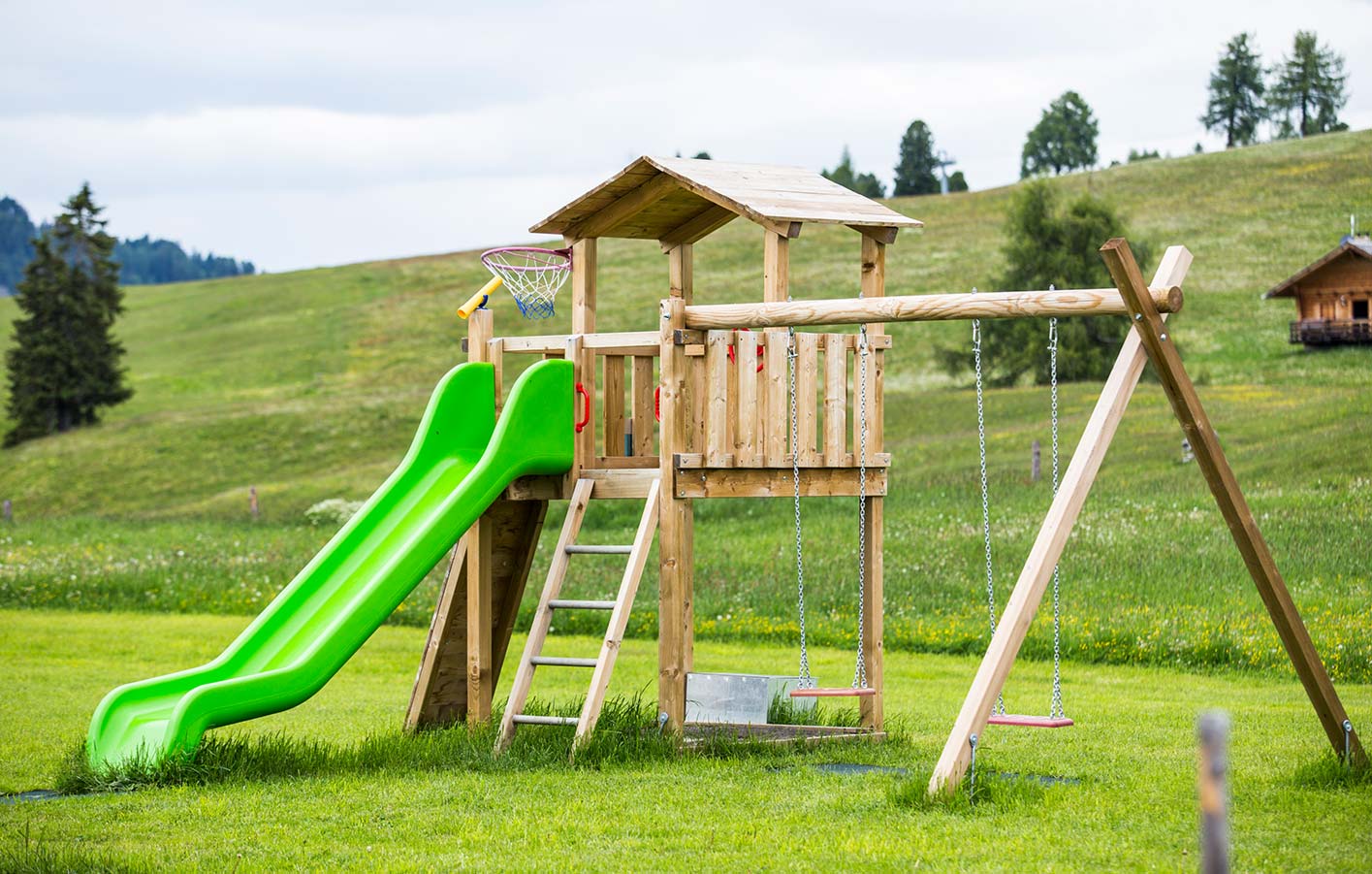 Ein Holzspielturm aus Holz mit Schaukel und Rutsche auf einer offenen Wiese