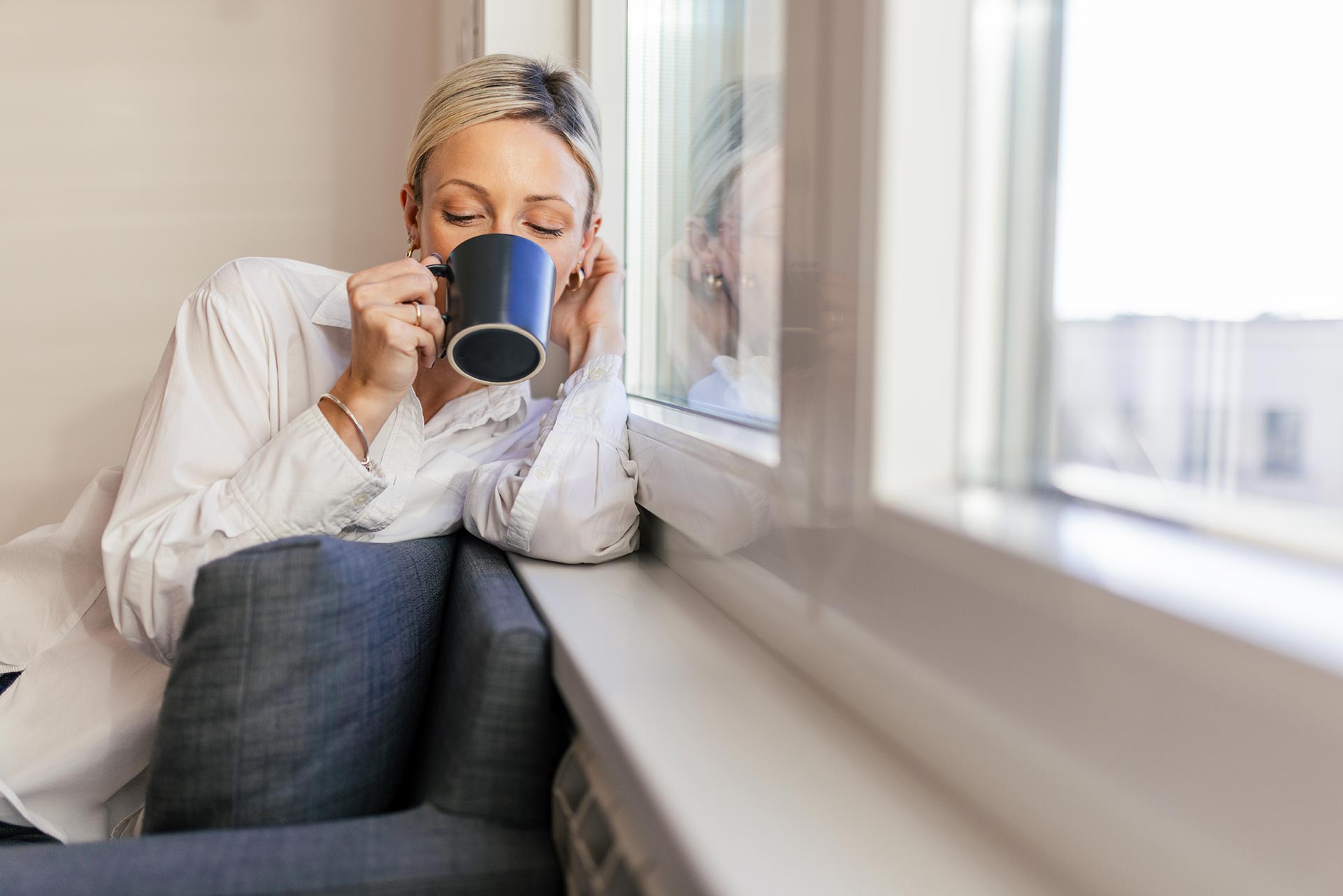 Fensterbänke für Innen und Außen bei Himmel & Weiss Frau lehnt mit Kaffeetasse am Fenster auf der Fensterbank